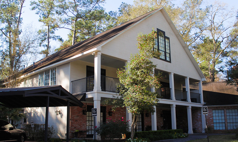 Image of the Living Proof Ministries building exterior, colonial-style architecture wiht two-tone brick and creamy-white facade surrounded by trimmed shrubbery and flowering trees.